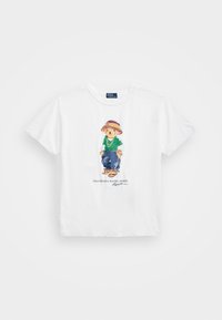 Weißes Baumwoll-T-Shirt mit einem bunten Cartoon-Bären-Design in lässiger Kleidung, komplett mit Strohhut und Sandalen, und ergänzt durch Text darunter.