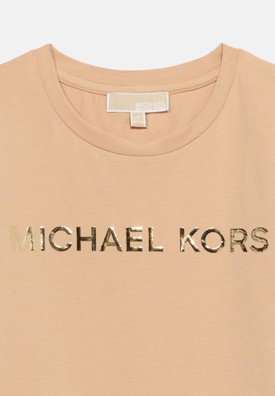 Μπεζ μπλούζα με στρογγυλή λαιμόκοψη, με λαμπερό χρυσό κείμενο "MICHAEL KORS" τυπωμένο στο στήθος και ορατή ετικέτα της μάρκας στο εσωτερικό του γιακά.