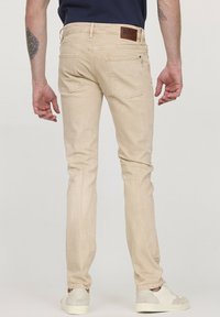Jean en denim beige avec une coupe slim, poches arrière et une patch en cuir à la taille. Portés avec des baskets de couleur claire.