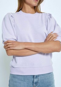 Lila sweatshirt med puffade kortärmar, ribbade muddar och fåll. Mjuk tyg och avslappnad passform, kombinerad med ljusblå denimjeans.