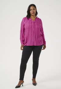 Fuchsia long-sleeve shirt with vertical white stripes and a buttoned placket, paired with black skinny jeans and pointed-toe heels.