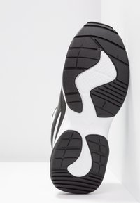 Musta-valkoinen urheilujalkineen pohja, jossa on kuvioitu rakenne. Siinä on uria pidon parantamiseksi ja erottuva kaareva muotoilu.