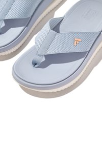 Ljusblå flip-flops med texturerade tygremmar och gummisula. Har en liten, orange logotyp på remmen. Släta ytor.