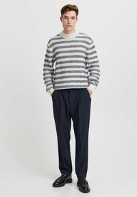Sweater features horizontal navy and cream stripes with a textured knit; paired with high-waisted, dark navy trousers and black shoes.