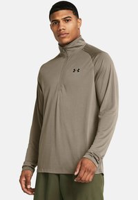 Hellbrauner, langärmliger Pullover mit Viertelreißverschluss aus glattem Material, mit einem dezenten Logo auf der Brust und kontrastierenden Seitenpaneelen.