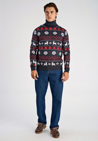 Marinblå tröja med polokrage prydd med vita snöflingor, renar och röda diamantmönster; kombinerad med blå jeans och bruna skor.