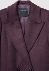 Cappotto di lana viola scuro con ampi revers, doppio petto e un'etichetta nera che riporta "CALLIOPE S" all'interno del colletto.