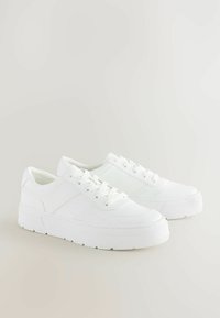 Sneakers bianchi con lacci, suola piatta, realizzati in materiale canvas, con una superficie liscia e dettagli di cucitura laterale sottili.