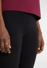 Maglietta corta color marrone scuro abbinata a leggings neri. La maglietta ha un orlo curvo e i leggings presentano una texture liscia e elastica.