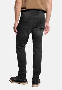 Svarta denimjeans med slim fit, med midjehöjd, två bakfickor och sömnadsdetaljer, i kombination med mörka skor.