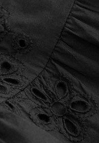 Tessuto nero con intricati ricami floreali e accenti di lavoro a giorno. Pieghe testurizzate corrono lungo un bordo, arricchendo il design.