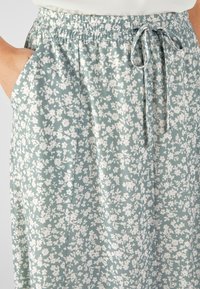 Gonna floreale azzurro chiaro realizzata in tessuto morbido. Presenta una vita arricciata, un laccio di regolazione e tasche laterali, con un delicato motivo di fiori bianchi.