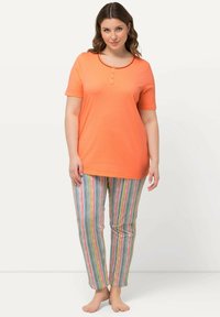 T-shirt in cotone arancione con collo rotondo e tre bottoni abbinato a pantaloni a righe multicolori con strisce rosse, verdi e blu.