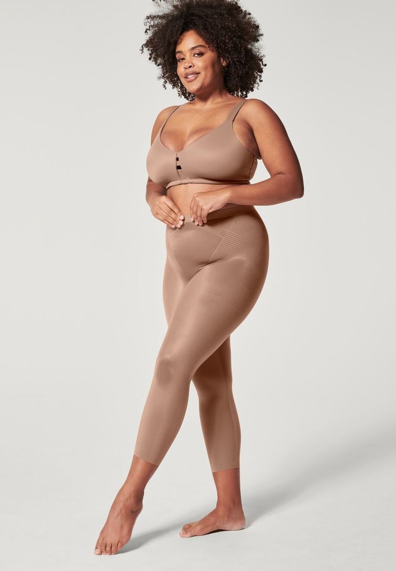 Beige sømløs bh med justerbare stropper og knappedetalj, parret med høyhente beige leggings med en glatt tekstur.