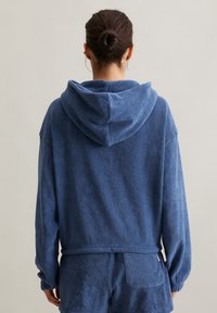 Felpa blu in spugna con vestibilità ampia, cappuccio grande e maniche lunghe. La texture è morbida; presenta un design semplice senza elementi hardware visibili.