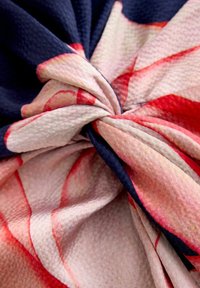 Tkanina w kwiatowy wzór w odcieniach granatu, różu i czerwieni, z fakturowaną powierzchnią i wiązaniem węzłowym na środku.