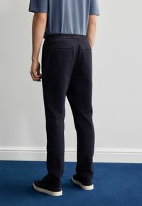 Mørkeblå sweatpants med en afslappet pasform, elastisk talje og to baglommer, sat sammen med en lyseblå kortærmet skjorte og sorte sneakers.