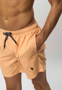 Perzikkleurige zwembroek van lichtgewicht stof, met een elastische tailleband, trekkoorddetail en zijzakken. Logo op het linkerbeen.
