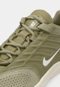 Ελιάς πράσινο Nike παπούτσι με υλικά από δίχτυ και σουέτ, μπεζ κορδόνια, λευκό λογότυπο swoosh και λεπτομερή ραφή σε ανοιχτό πέλμα.