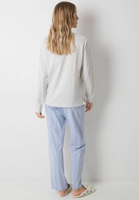 Lichtgrijs langemouwen shirt, blauwe gestreepte broek met kleine blauwe stippen, ontspannen pasvorm, gedragen met instap-schoenen, tegen een effen achtergrond.