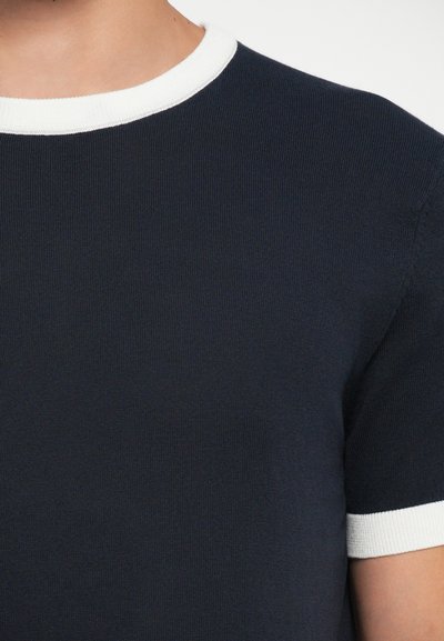 T-shirt azul-marinho com uma textura em renda, apresentando um decote redondo branco e mangas curtas, enfatizando um design simples e clássico.