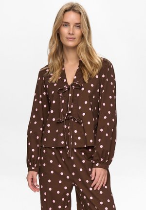 Blouse marron à manches longues avec des pois roses, encolure en V et détail de nouage à l'avant. Poignets élastiqués et ourlet raccourci. Texture de tissu lisse.