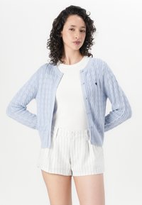 Light blue cable-knit cardigan with a round neckline and button closure, paired with white striped shorts and a fitted white top.