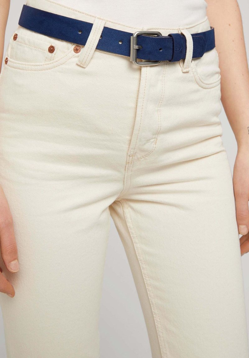 Cinturón de cuero azul marino con una hebilla de plata, combinado con unos jeans de mezclilla blanco roto, que presentan costuras visibles y remaches de cobre.