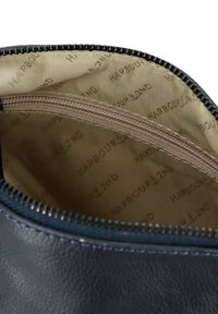 Vista interna di una borsa in pelle blu navy che mostra una fodera in tessuto beige stampata con "HARBOUR 2ND" e una tasca con zip beige chiusa all'interno.