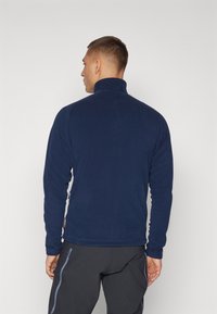 Navy fleece jacket with high collar, long sleeves, and a smooth texture. Features a logo tag on the hem and minimalistic design.