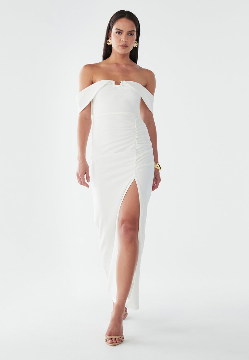 Biely off-the-shoulder šaty s riasenými detailami, vysokým rozparkom, priliehajúcim strihom a mäkkým elastickým materiálom. Minimalistický elegantný štýl.