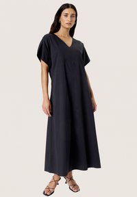 Black, loose-fitting maxi dress with a V-neck and short sleeves, featuring vertical seams for structure. Lightweight fabric, smooth texture.
