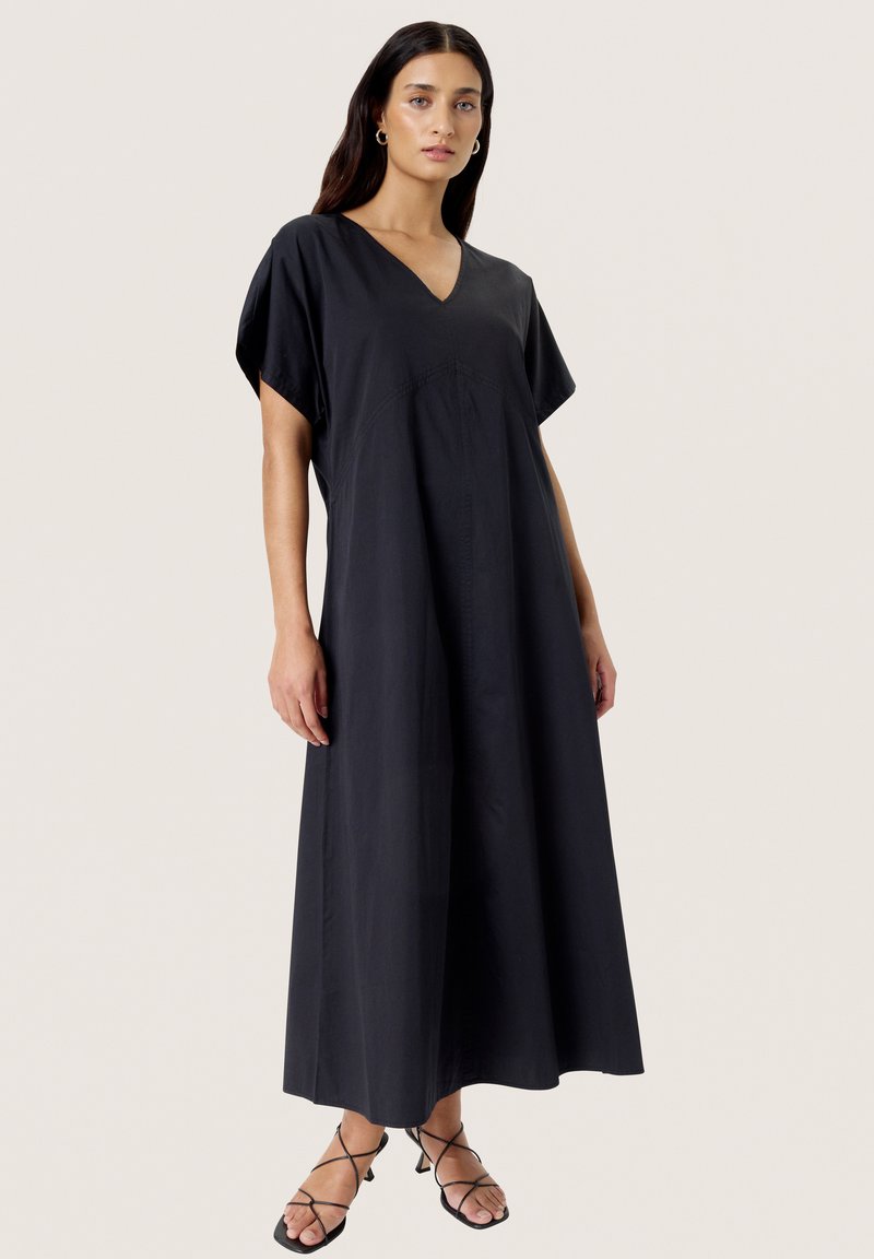 Black, loose-fitting maxi dress with a V-neck and short sleeves, featuring vertical seams for structure. Lightweight fabric, smooth texture.