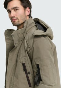 Khaki parka bunda s kapucňou, viacerými zipsovými vreckami a hladkou textúrou. Navrhnutá s moderným strihom a odolným materiálom.