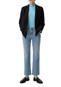 Blazer noir sur un col roulé bleu clair, associé à un jean droit bleu clair et des mocassins noirs. Tissu lisse et coupe ajustée.