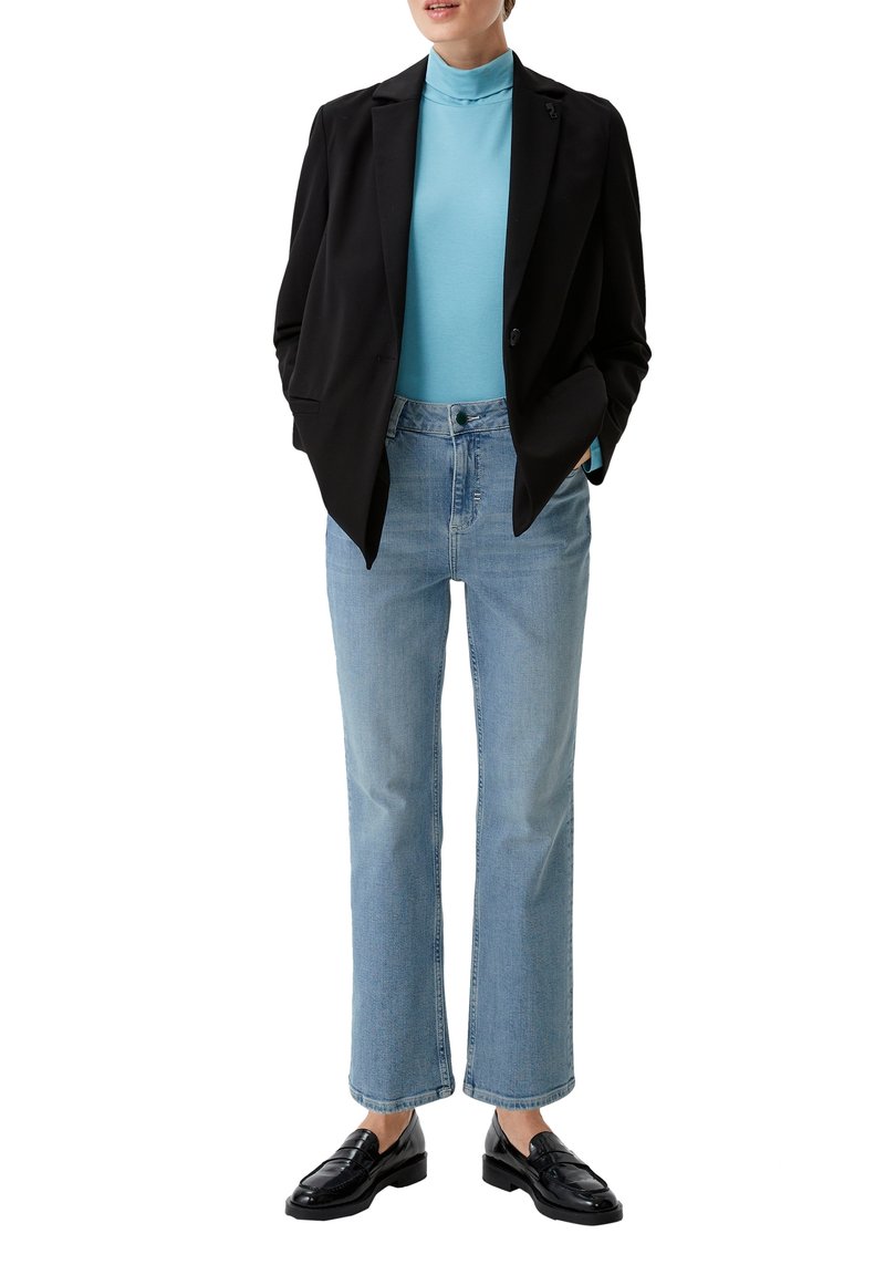 Blazer noir sur un col roulé bleu clair, associé à un jean droit bleu clair et des mocassins noirs. Tissu lisse et coupe ajustée.