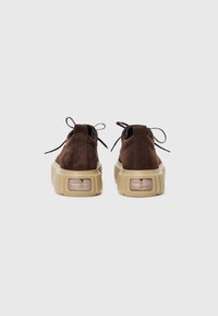 Chaussures en daim marron avec une épaisse semelle en caoutchouc beige, dotées d'un bout arrondi et de lacets décoratifs à l'arrière pour la fermeture.