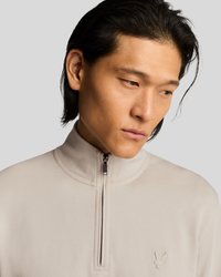 Μπεζ ανοιχτό μπεζ πουλόβερ με μισό φερμουάρ, σε απαλό υφή υφάσματος με ανυψωμένο γιακά και κεντημένη λεπτομέρεια λογότυπου στο στήθος.