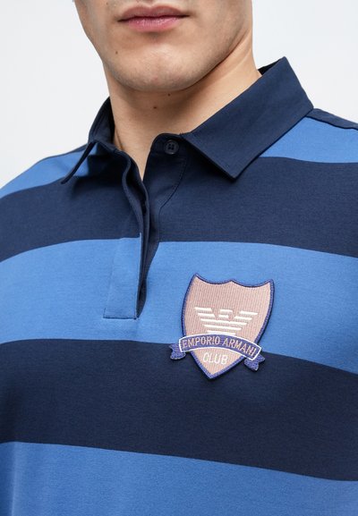 Μπλουζάκι πόλο με οριζόντιες ρίγες σε ναυτικό και ανοιχτό μπλε, γιακά και κεντητό σήμα Emporio Armani Club στο αριστερό στήθος.
