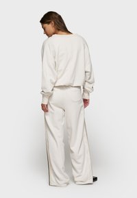 Crème-kleurige, oversized trui met verlaagde schouders, gecombineerd met bijpassende wijde broek met zijstrepen en een achterzak.