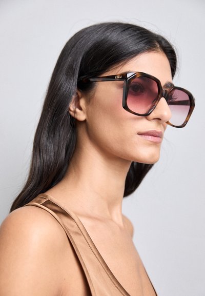 Large, square sunglasses with a brown tortoiseshell frame and gradient pink lenses. Features a gold logo accent on the temple.
