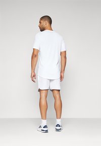 T-shirt atletica bianca a maniche corte, abbinata a pantaloni corti bianchi. Marchio visibile sui pantaloni. Tessuto liscio e leggero, design semplice.