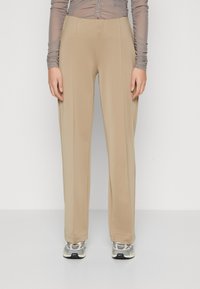 Pantaloni bej cu talie înaltă, cu o textură netedă, picioare largi și o croială ajustată. Asortați cu adidași gri și albi.