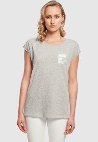 Camiseta gris de manga corta con cuello redondo y texto impreso "ESPERANDO EL VIERNES" en el área del pecho izquierdo. Tejido suave, corte holgado.