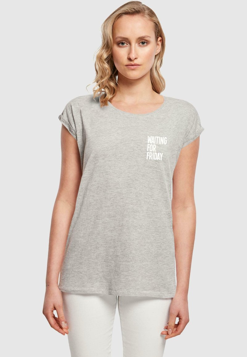 Camiseta gris de manga corta con cuello redondo y texto impreso "ESPERANDO EL VIERNES" en el área del pecho izquierdo. Tejido suave, corte holgado.
