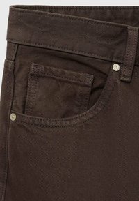 Brown denim pants with a textured finish, featuring a front pocket and metal hardware accents. Constructed with a sturdy waistband.