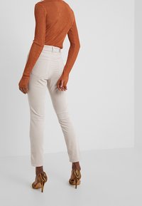 Rippentrikots in Orange mit langen Ärmeln, beige, figurbetonte Hose und gestreifte High Heels mit spitzem Zeh. Fokus auf strukturierten Stoffen und kräftigen Mustern.