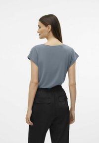 Top gris de manga corta con un corte relajado, que presenta un escote amplio. Combinado con pantalones negros de talle alto con bolsillos traseros.