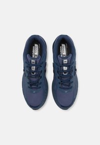 Marinblå löparskor med mesh-överdela, snören och förstärkta detaljer; har en tjock gummisul och en logotyp på tungan.