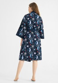 Marinblå badrock med himmelska mönster, inklusive månar och stjärnor. Mjuk tyg, bälte i midjan och vida ärmar. Halvlång design.